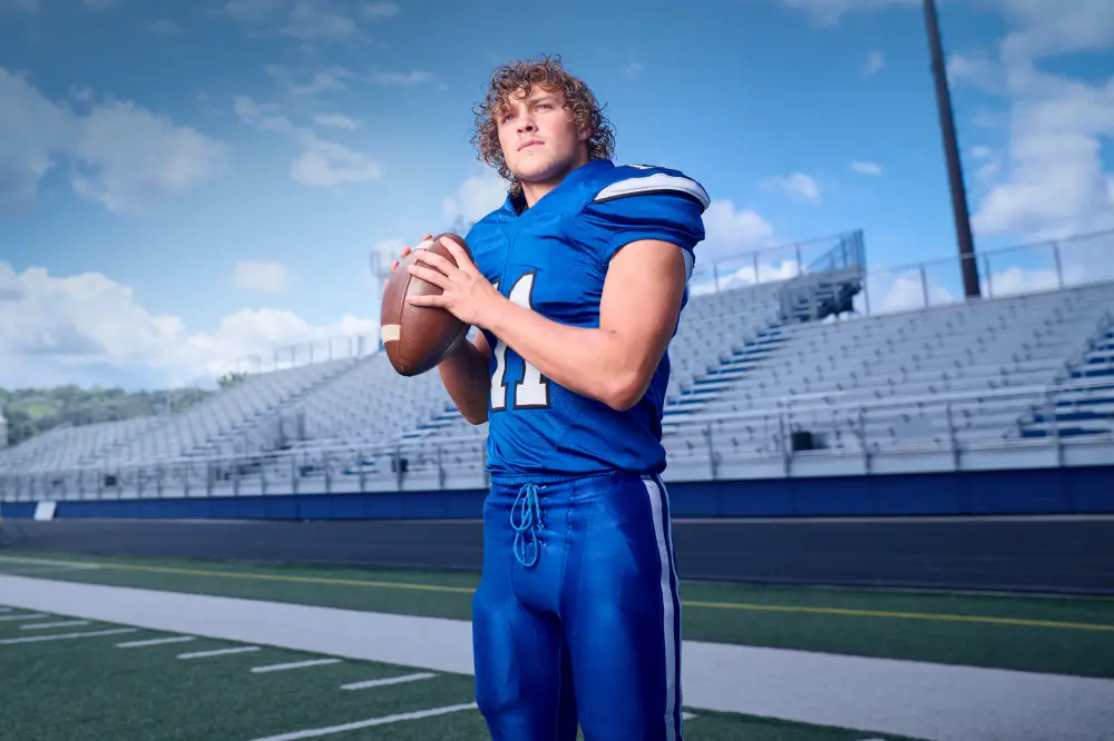 Coen Patient Story A sports medicine patient stands confidently on a football field dressed in a blue uniform, holding a football with both hands.
