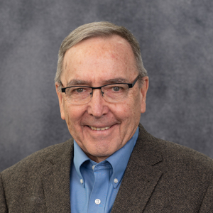 Jim Crabtree is smiling in a formal headshot in a navy shirt & a tan blazer.