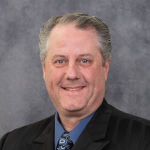 Sean Kallner smiling in his headshot wearing a navy shirt and a black blazer.