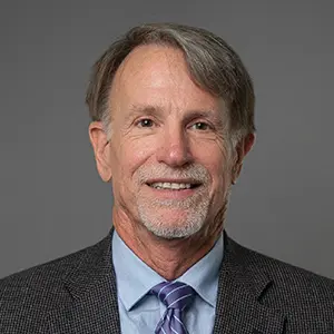 Headshot of Brian Ream in a dark checkered suit jacket, light blue shirt, and purple striped tie.