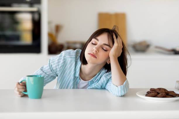 A young woman feeling tired at her kitchen counter.