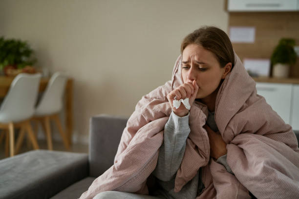 A lady wrapped in a blanket, sick, coughing into a tissue.