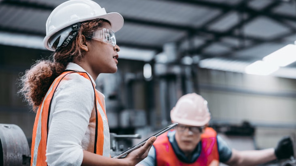 Two workers, in safety gear, working in a factory.