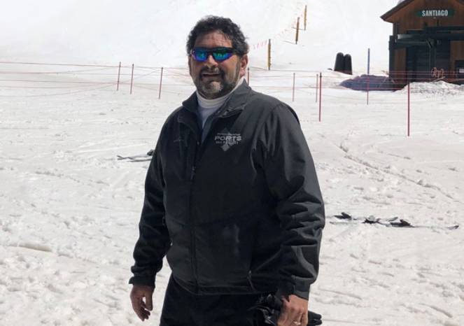 john-ross-663 John Ross, an Adena Health patient, stands smiling in a snowy ski area wearing a dark jacket and sunglasses, with ski equipment in hand.