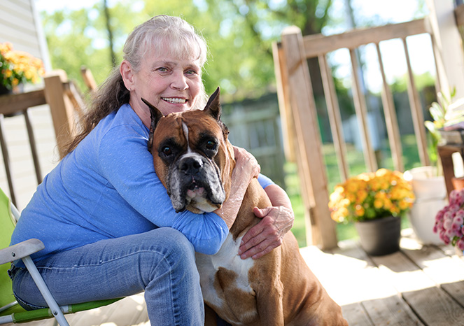 kim-riffle Kim Riffle, an Adena Health patient, smiles while hugging her large brown and white dog on a sunny porch surrounded by flowers.